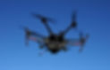 A drone with multiple rotors flies against a bright blue sky