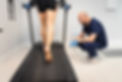 Podiatrist kneeling to track and film a patient walking on a treadmill during a clinical gait analysis