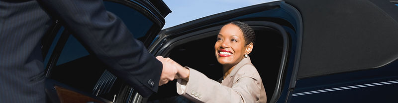 chauffeur holding black car door open for female passenger getting in.jpg
