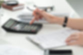 A woman's hand points at a calculator resting on a desk, indicating a focus on calculations or financial tasks