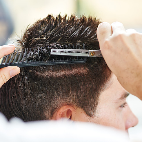 A hairdresser giving a haircut to a young man at a salon