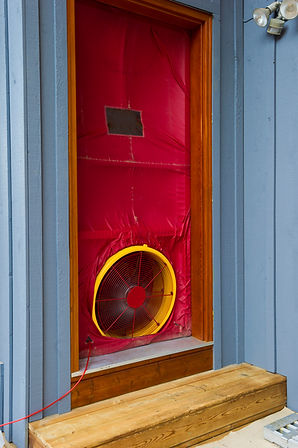 A red door cover with a yellow fan is installed in a wooden doorframe with blue siding