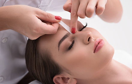 Esthetician shaping and waxing a client’s eyebrows during a brow design service.