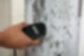 Close-up of a person's hand using a device to survey a damp interior wall