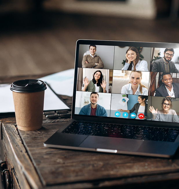 Diverse group of business professionals engaged in an interactive online video meeting on a laptop next to a paper coffee travel cup on a wooden table