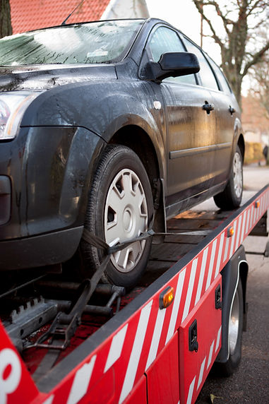 A car is being towed, secured with straps on a flatbed tow truck