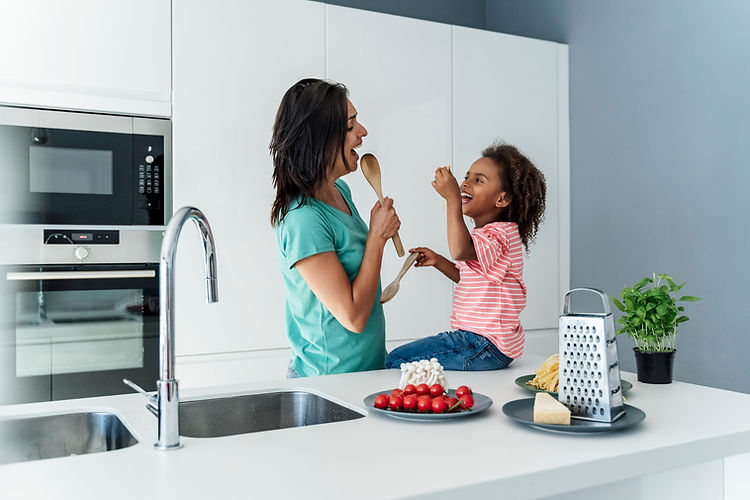 Mother and daughter singing with wooden spoons in the modern kitchen.