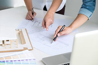 Two people examine architectural blueprints on a white table, pointing and discussing