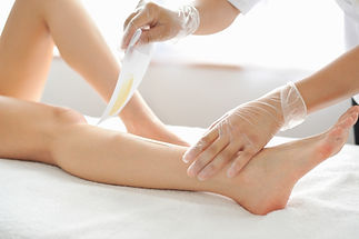 Therapist in gloves preparing to pull a wax strip off a client's lower leg on a beauty couch