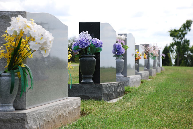 Headstones with colorful flowers in vases line a cemetery on a green lawn