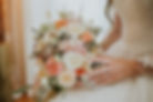 Bride holding floral bouquet with peach, white, and green blossoms up close