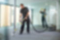 A man uses a vacuum cleaner on the carpet in a modern office space