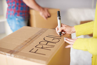 Close-up of a person writing "FRAGILE" on a cardboard box with a marker