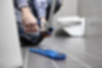 A person kneels on a tiled bathroom floor, repairing a pipe with pliers