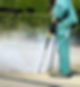 Worker in green overalls using a high-pressure cleaner on pavement