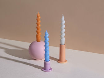 Three twisted candles in pastel holders against a beige background