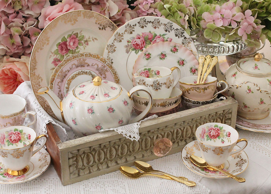 Display of vintage teacups, plates and teapots in a distressed wood drawer with lace doili