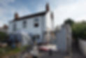A white two-story house with a chimney, surrounded by construction materials and scaffolding