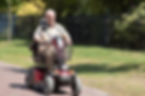 An elderly man rides a red mobility scooter on a sunny day