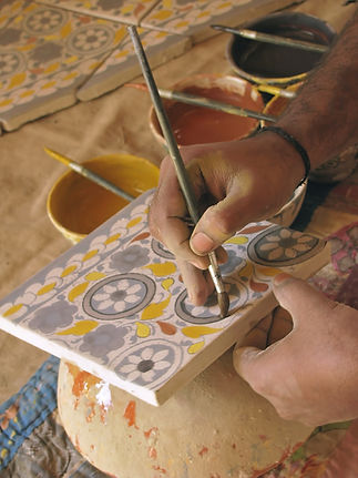 An artisan uses a fine paintbrush to apply gray pigment to a ceramic tile