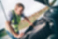 A person in a reflective vest examines the engine of a car