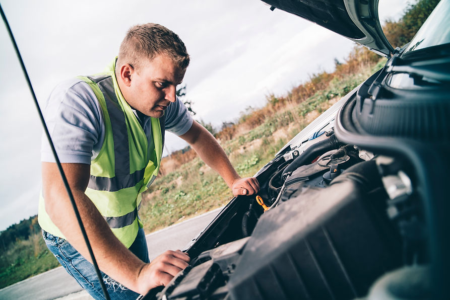 A man in a reflective vest inspects a car engine on a rural roadside