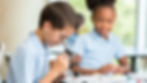 Boy using a microscope in a science class with a curious female peer looking on