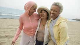 A diverse group of three smiling women walking on a beach.