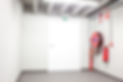 Empty room with white door, exit sign, fire hose reel, and extinguishers on wall