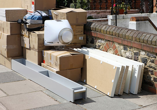 Open and sealed cardboard moving boxes stacked outdoors next to a brick wall during a domestic relocation