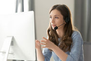 Young woman with headset looking at computer, assisting customers.