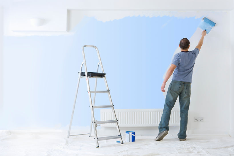 Painter in a gray t-shirt painting a wall with a roller in a brightly lit room