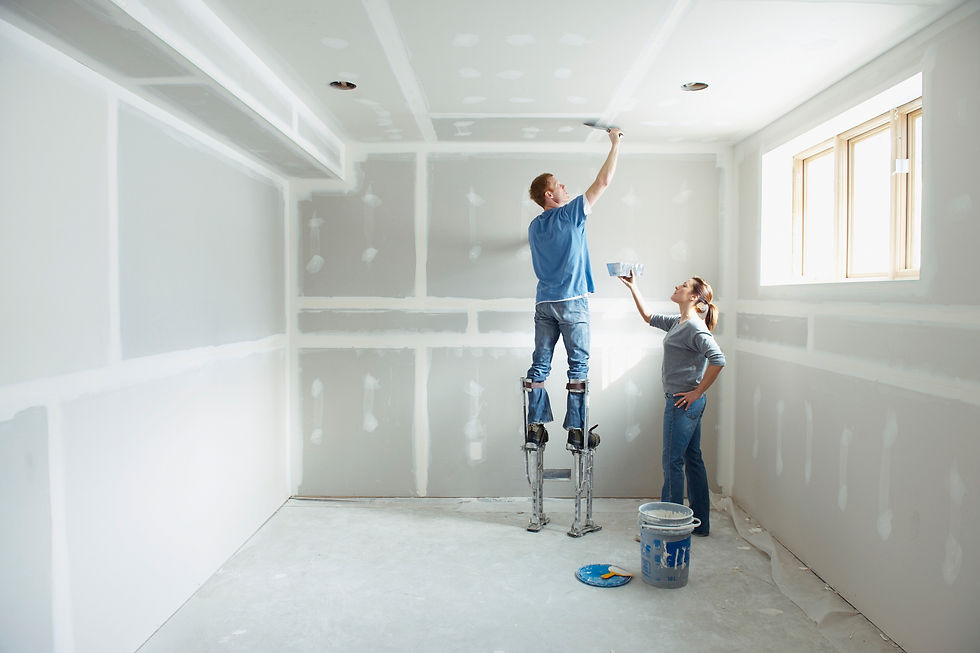 Couple finishing a drywall ceiling in an unfinished room, with the man standing on drywall stilts.
