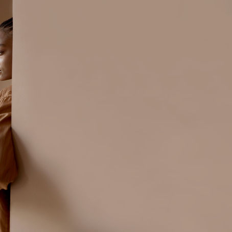Person with braided hair in a tan shirt looks seriously at the camera. Beige background with a calm, introspective mood.