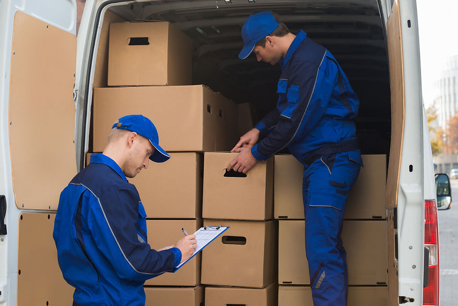 Delivery man unloading cardboard boxes from truck while colleague writing on clipboard