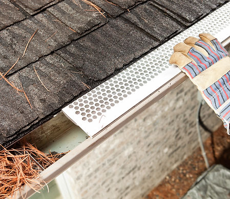 A worker, with gloved hands, is installing a gutter guard leaf shield on a house roof