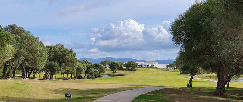 Green golf course with trees, sand bunkers, and distant hills.