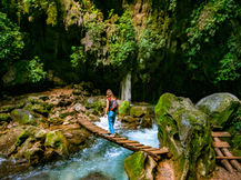 person crossing water on a small wooden bridge