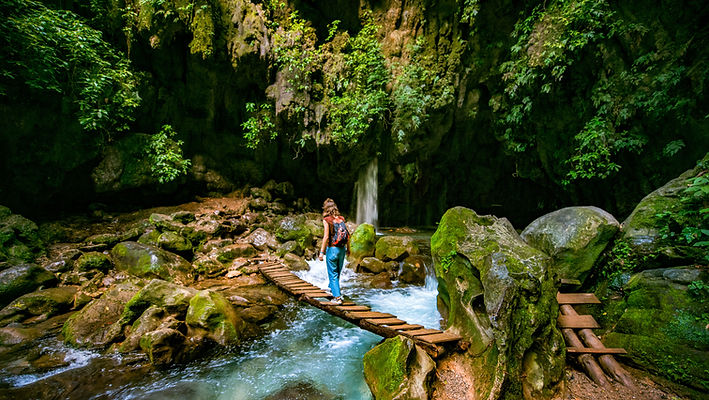 Woman crossing a narrow wooden bridge over a river in a forest