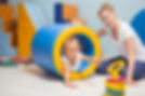 A woman and a young girl play in a colorful indoor playroom