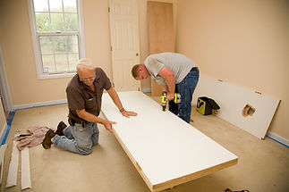 Two men assemble a white door on the floor of a beige room