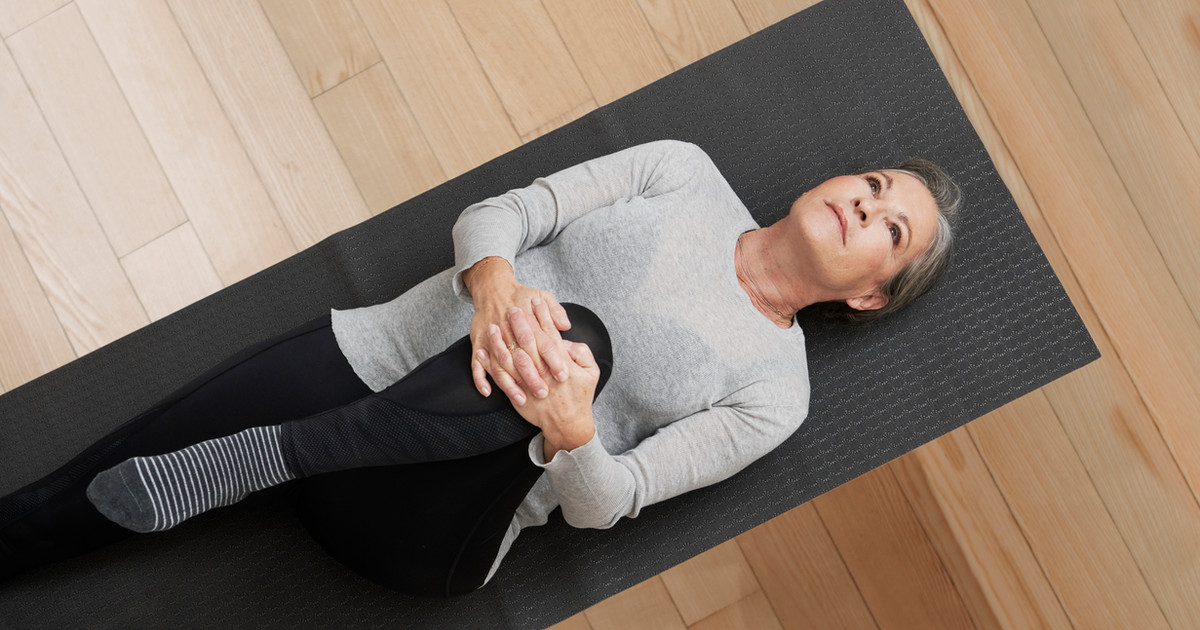 A person doing a gentle stretch in a bright living room, with a yoga mat and water bottle nearby, conveying calm self-directed movement.