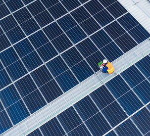 Aerial view of a man inspecting solar panels on a galvanised roof.
