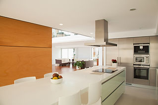 Modern open-concept kitchen and living area; white island with fruit bowl, sleek stove, and chairs in foreground
