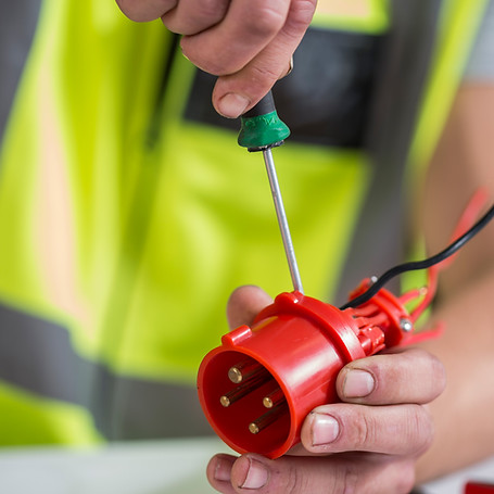 Man uses a screwdriver to adjust a red industrial plug with wires
