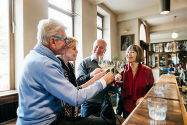 A group of senior friends smiling and raising glasses of wine for a toast at a bar during a BACCO event.