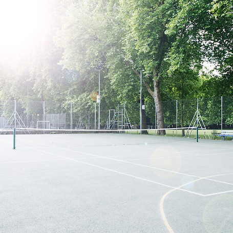 A tennis court with empty nets, surrounded by lush green trees