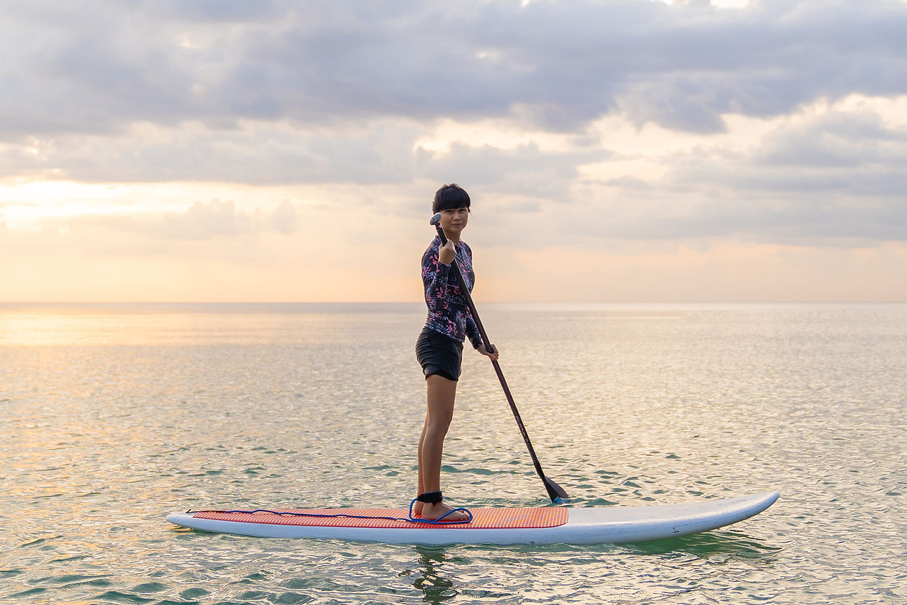 a Woman paddleboarding on the Ocean with a cloudy sky above her