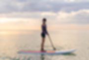 a Woman paddleboarding on the Ocean with a cloudy sky above her