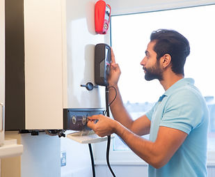 A young male engineer is standing checking the gas central heating boiler